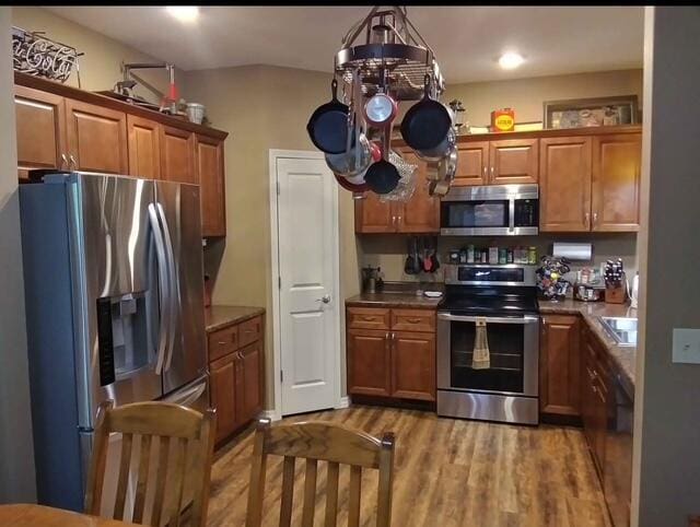 kitchen featuring brown cabinetry, appliances with stainless steel finishes, an inviting chandelier, light wood-style floors, and a sink