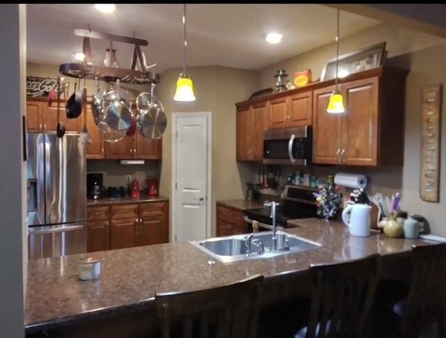 kitchen featuring pendant lighting, appliances with stainless steel finishes, brown cabinetry, a sink, and a peninsula