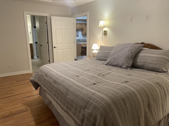 bedroom featuring ensuite bathroom, light wood-style flooring, and baseboards