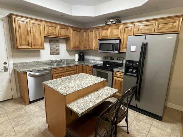 kitchen with baseboards, appliances with stainless steel finishes, brown cabinets, a center island, and a sink