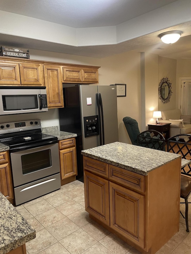 kitchen featuring brown cabinetry, a kitchen island, light stone counters, open floor plan, and stainless steel appliances