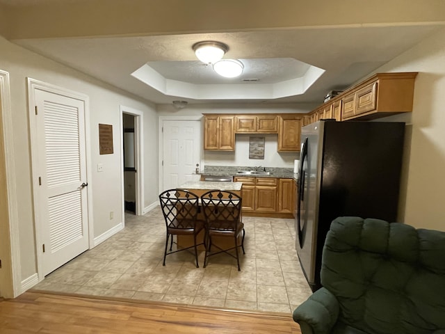 kitchen featuring a raised ceiling, a center island, freestanding refrigerator, light wood-type flooring, and a sink