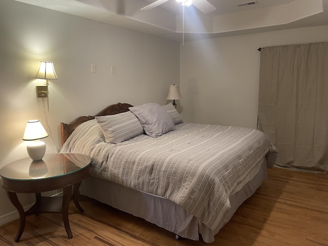 bedroom featuring a tray ceiling, wood finished floors, and visible vents