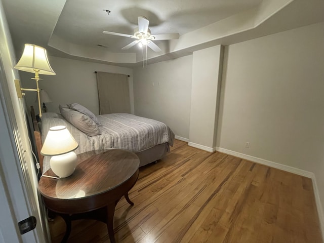 bedroom with light wood finished floors, a tray ceiling, and baseboards