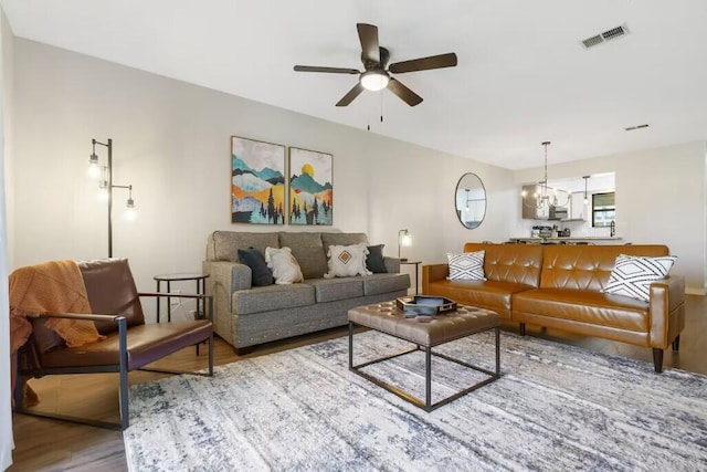 living area with a ceiling fan, visible vents, and wood finished floors