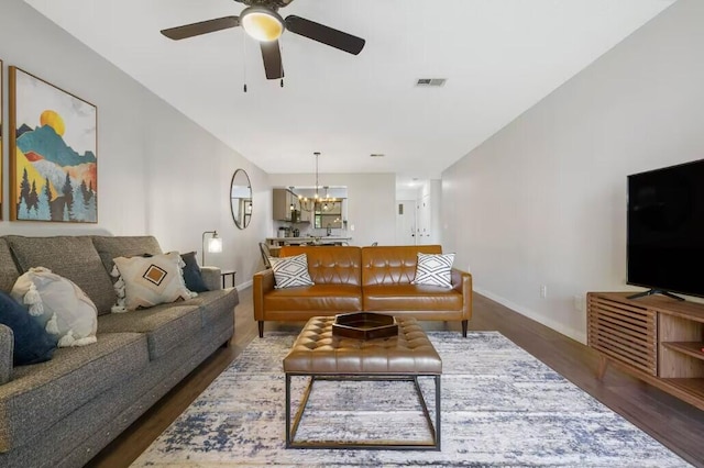 living room with baseboards, visible vents, wood finished floors, and ceiling fan with notable chandelier