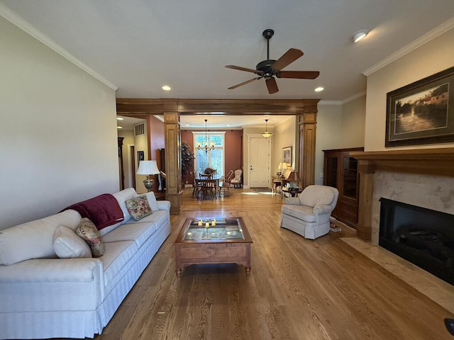 living area with wood finished floors, visible vents, a premium fireplace, ornamental molding, and ceiling fan with notable chandelier