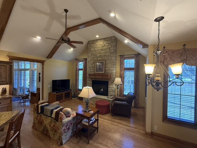 living room with ceiling fan with notable chandelier, wood finished floors, a stone fireplace, baseboards, and vaulted ceiling with beams