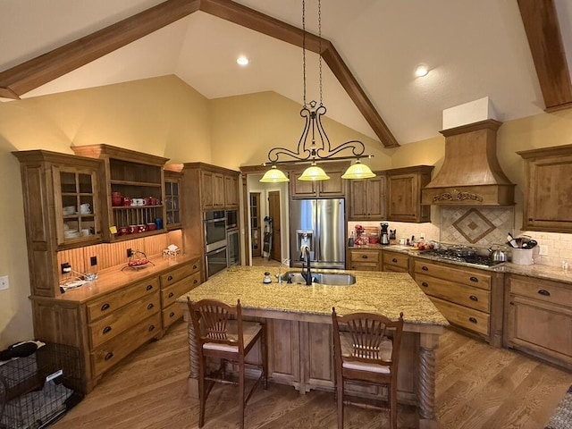 kitchen with a sink, premium range hood, wood finished floors, stainless steel appliances, and a kitchen island with sink