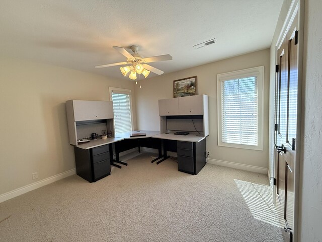 office featuring a ceiling fan, visible vents, baseboards, a textured ceiling, and light colored carpet