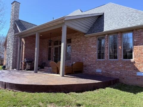 rear view of house with crawl space, a patio, brick siding, and a chimney