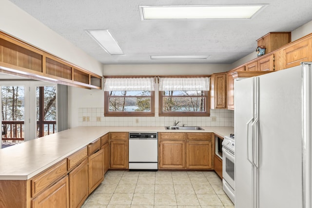 kitchen featuring a peninsula, white appliances, a sink, and light countertops