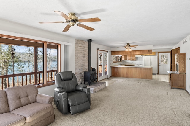 living room with a wood stove, ceiling fan, light carpet, and a textured ceiling