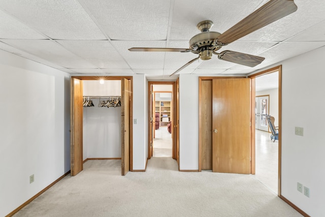 unfurnished bedroom featuring light carpet, ceiling fan, a drop ceiling, and baseboards