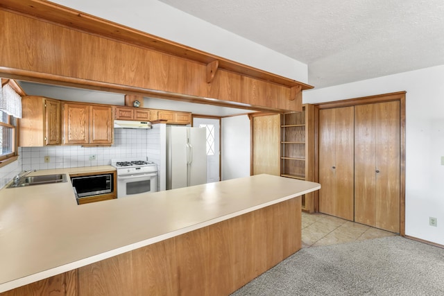 kitchen with under cabinet range hood, a peninsula, white appliances, a sink, and light countertops