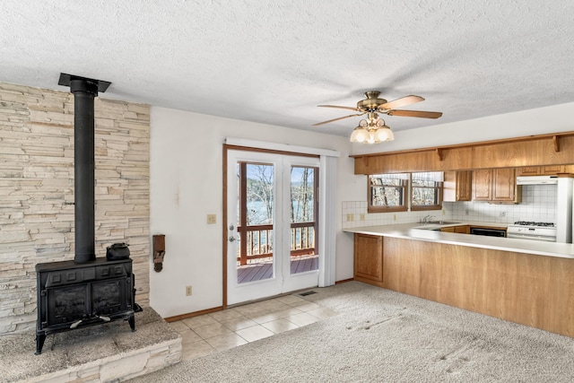 kitchen with brown cabinets, white gas stove, decorative backsplash, a wood stove, and under cabinet range hood