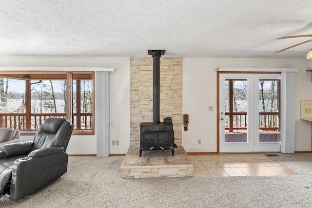 tiled living area with a textured ceiling, carpet, a wood stove, and a ceiling fan