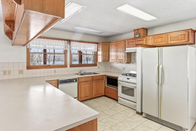 kitchen with light countertops, decorative backsplash, a sink, white appliances, and under cabinet range hood