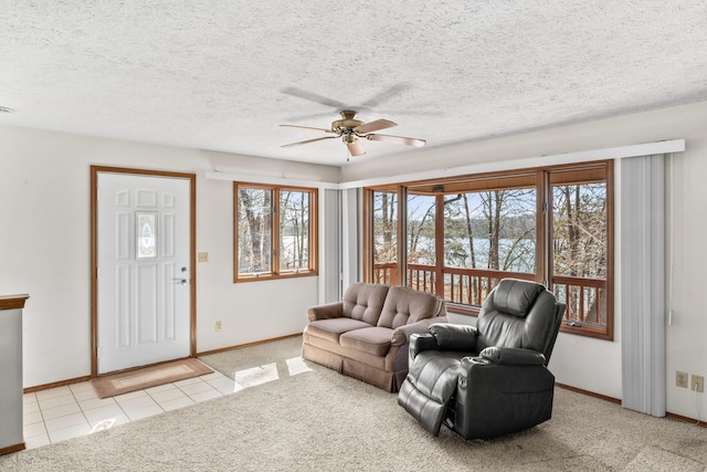 living room featuring carpet floors, a ceiling fan, a textured ceiling, baseboards, and tile patterned floors