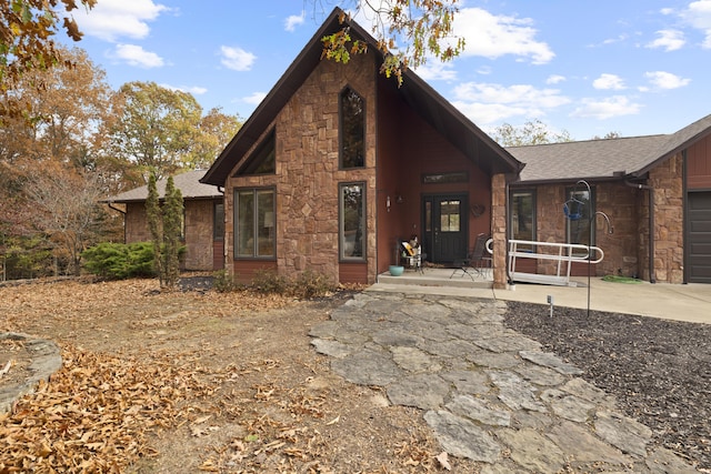 chalet / cabin featuring an attached garage, stone siding, roof with shingles, and concrete driveway