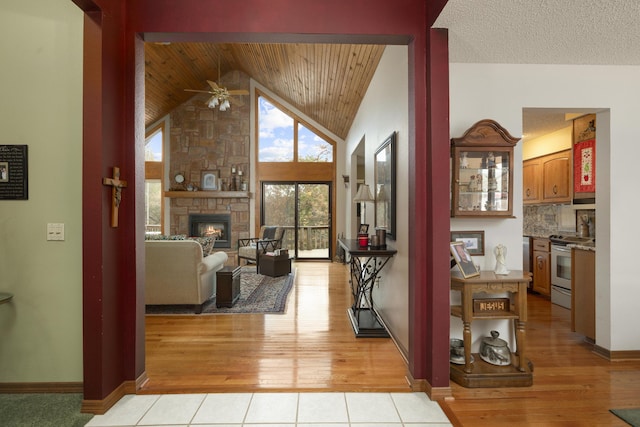 interior space featuring light tile patterned floors, baseboards, wooden ceiling, a fireplace, and high vaulted ceiling