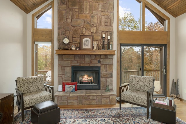 living area with plenty of natural light, a stone fireplace, wooden ceiling, and wood finished floors