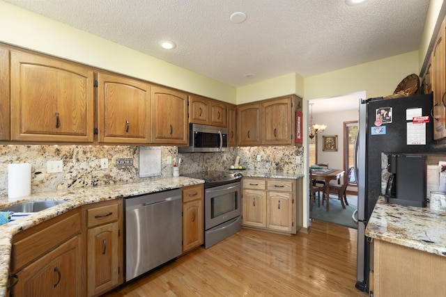 kitchen with stainless steel appliances, light wood-type flooring, backsplash, and a notable chandelier