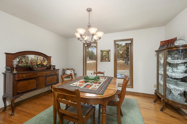 dining area featuring a chandelier, a textured ceiling, light wood-type flooring, and baseboards