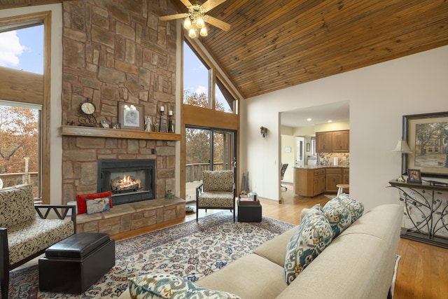 living room featuring light wood-style floors, wood ceiling, a stone fireplace, high vaulted ceiling, and baseboards