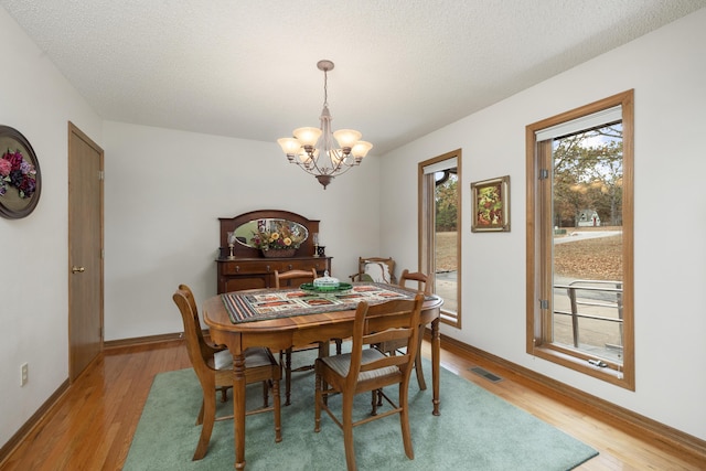 dining room with light wood finished floors, visible vents, a textured ceiling, a chandelier, and baseboards