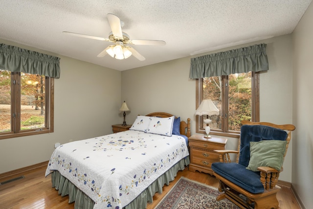 bedroom featuring a textured ceiling, wood finished floors, visible vents, baseboards, and a ceiling fan