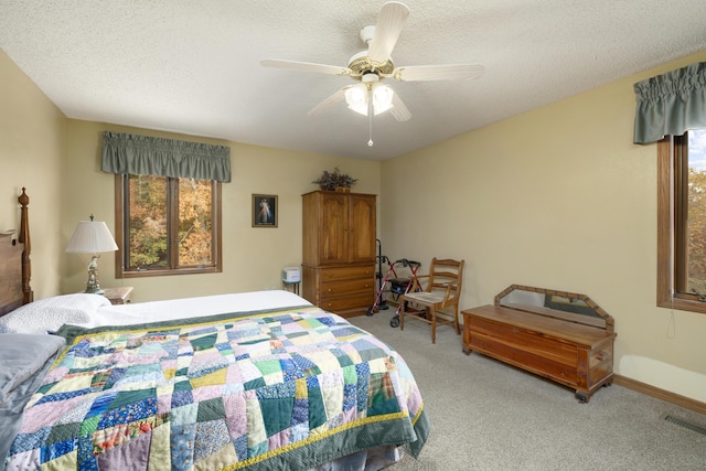 carpeted bedroom featuring ceiling fan, multiple windows, visible vents, and a textured ceiling