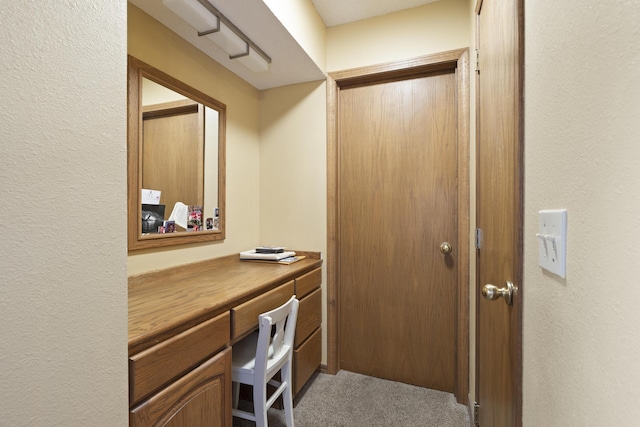 carpeted home office featuring a textured wall and built in study area