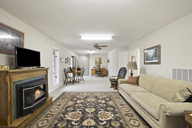 living room with visible vents, a ceiling fan, a glass covered fireplace, a textured ceiling, and carpet flooring