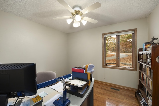 office space featuring baseboards, visible vents, ceiling fan, wood finished floors, and a textured ceiling