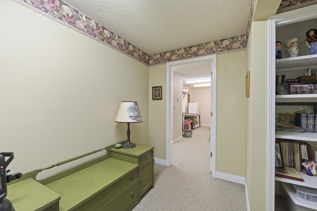 hall with a textured ceiling, baseboards, and light colored carpet