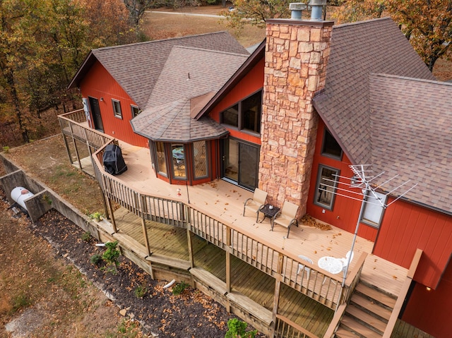 rear view of house featuring a deck, roof with shingles, and a chimney