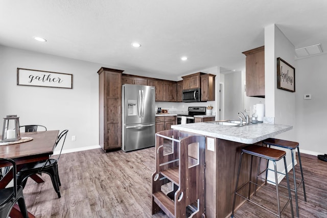 kitchen with a peninsula, a sink, a kitchen breakfast bar, light countertops, and appliances with stainless steel finishes