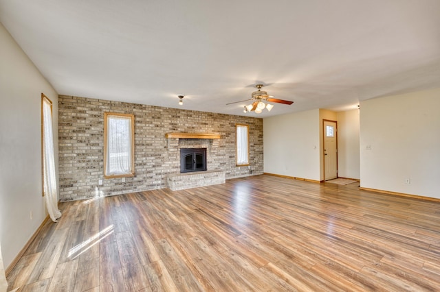 unfurnished living room featuring ceiling fan, brick wall, a fireplace, and wood finished floors