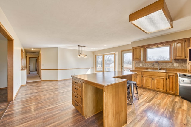 kitchen featuring tasteful backsplash, dishwasher, a kitchen island, light wood-style floors, and a sink