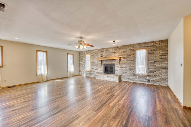 unfurnished living room with wood finished floors, visible vents, baseboards, a ceiling fan, and a brick fireplace