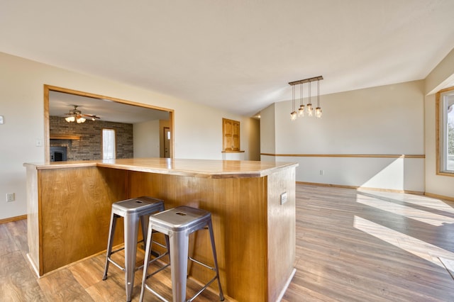 kitchen featuring a fireplace, light wood-style floors, open floor plan, ceiling fan, and baseboards