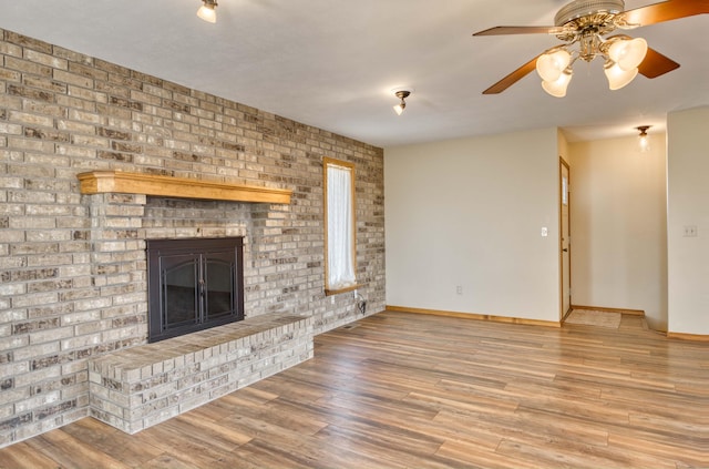 unfurnished living room with a brick fireplace, ceiling fan, baseboards, and wood finished floors