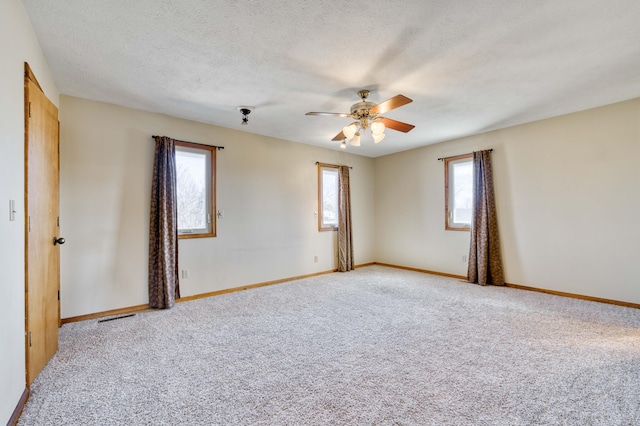 carpeted spare room featuring a textured ceiling, visible vents, a ceiling fan, and baseboards