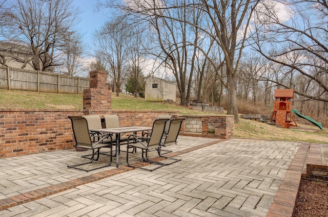 view of patio / terrace featuring outdoor dining space, a playground, fence, and an outdoor structure