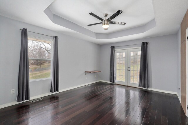 empty room with french doors, a raised ceiling, visible vents, a healthy amount of sunlight, and wood finished floors