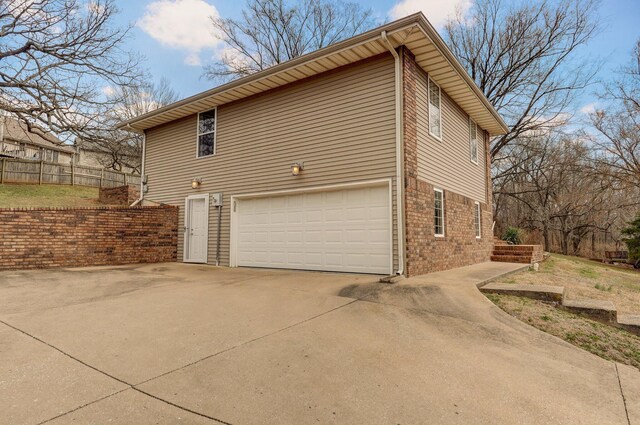 view of home's exterior with a garage, concrete driveway, brick siding, and fence