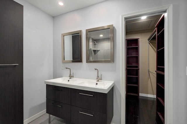 bathroom featuring double vanity, baseboards, a walk in closet, and a sink