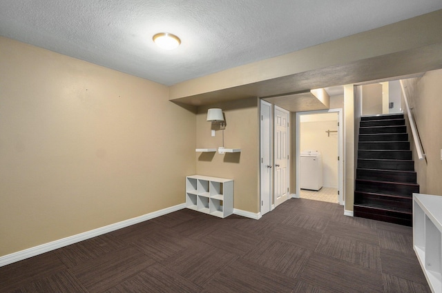 finished below grade area featuring a textured ceiling, baseboards, stairs, dark colored carpet, and washer / dryer