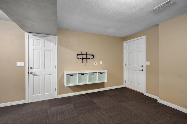 interior space featuring visible vents, a textured ceiling, dark carpet, and baseboards